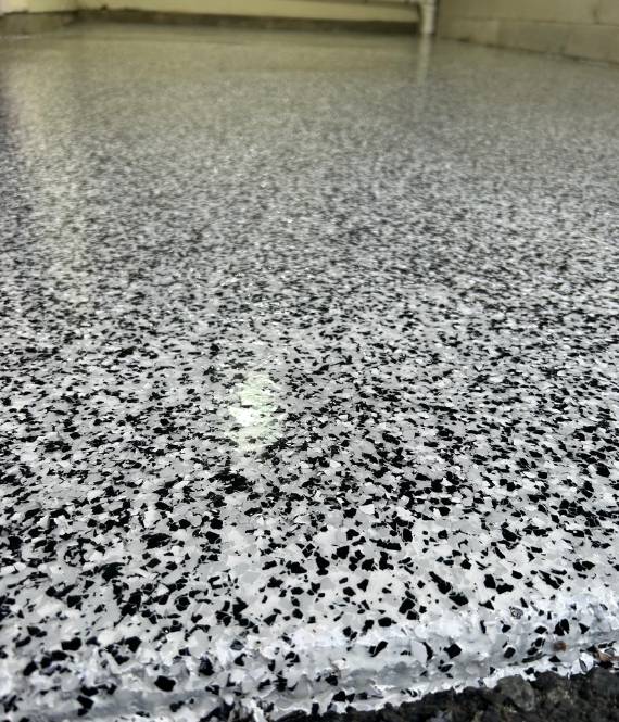 http://A%20flake%20epoxy%20floor%20with%20a%20black%20and%20white%20speckled%20pattern,%20prominently%20displaying%20white%20spots%20throughout.