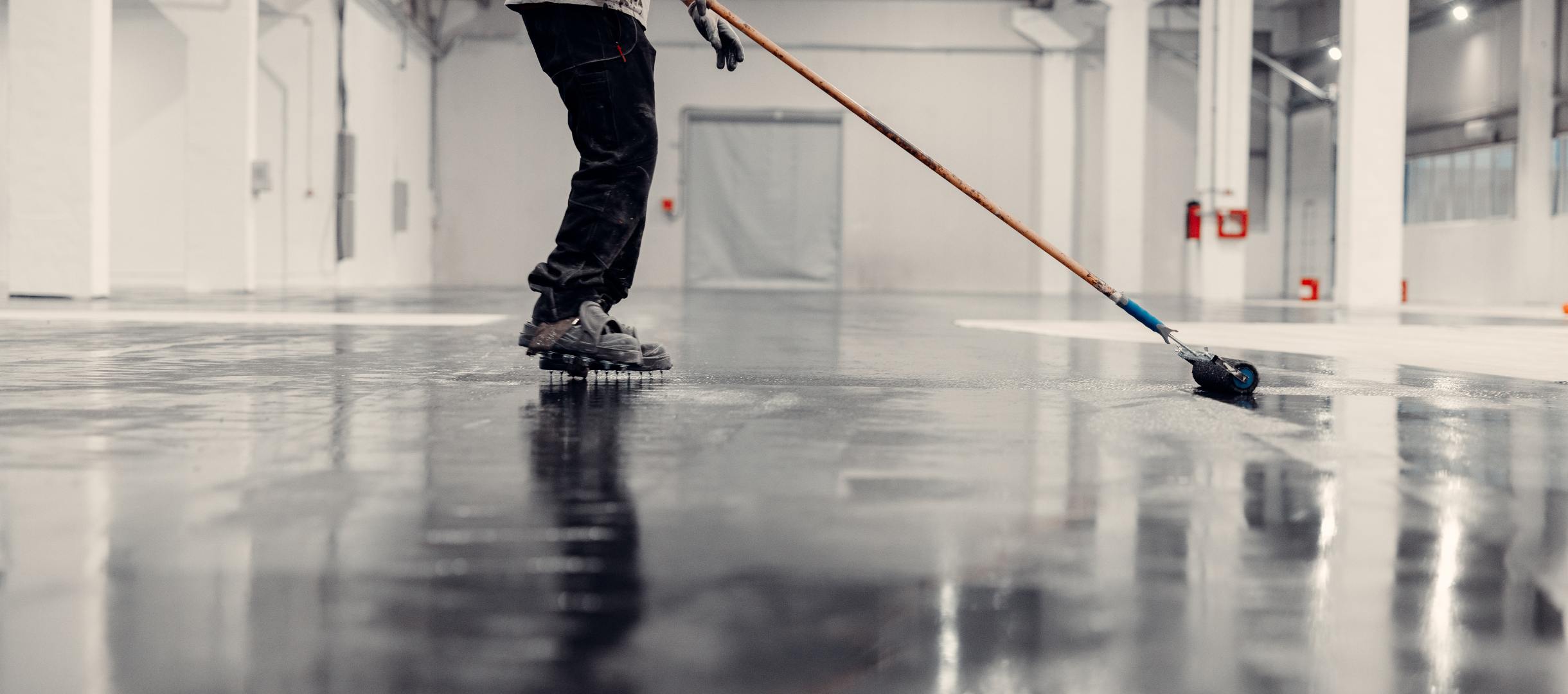 Worker applying black epoxy resin in a big open empty warehouse